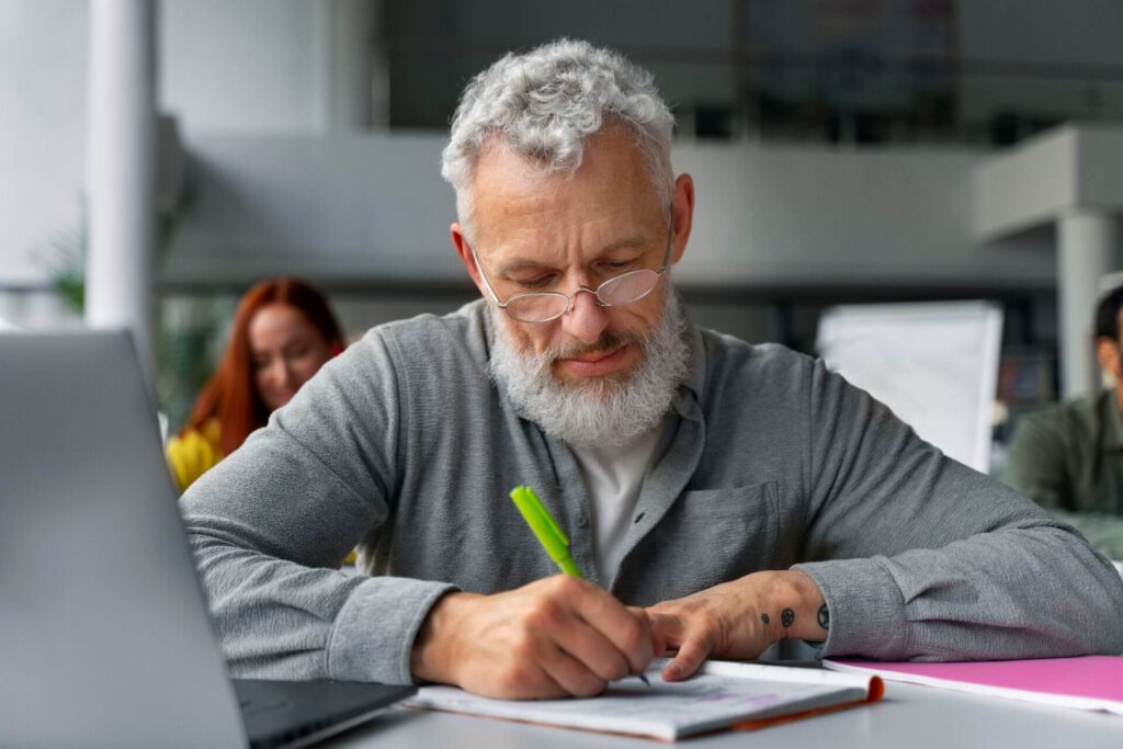 Homem mais velho estudando intensamente com um caderno em frente a um laptop, simbolizando o aprendizado contínuo para as profissões do futuro